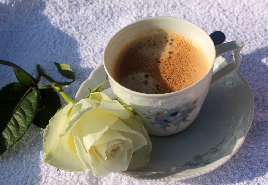 カップに入ったコーヒーと白い一輪の薔薇